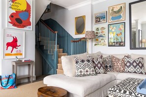 Un salon avec un escalier, un canapé agrémenté de coussins à motifs et divers tableaux encadrés accrochés aux murs.