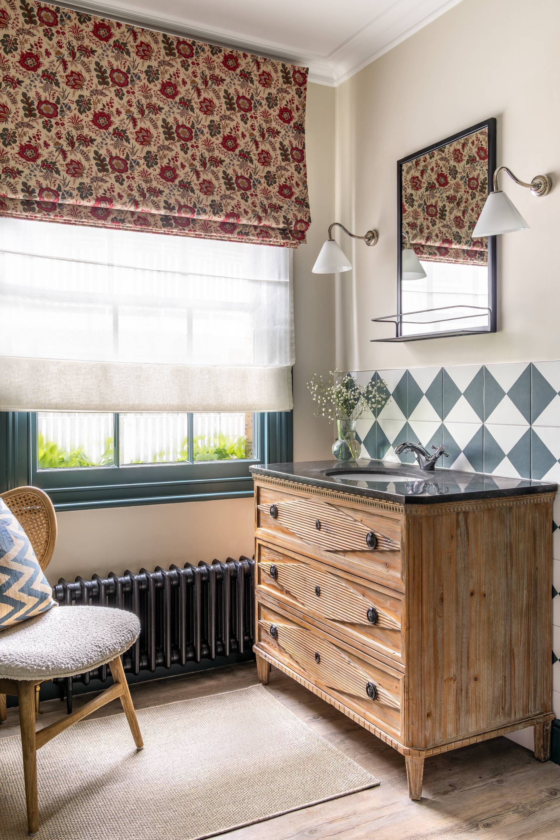 A bathroom with a wooden cabinet, a mirror, a window with a floral valance, and a radiator.