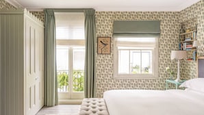 A bedroom with a bed, a window with curtains, a bedside table, and a bookshelf.