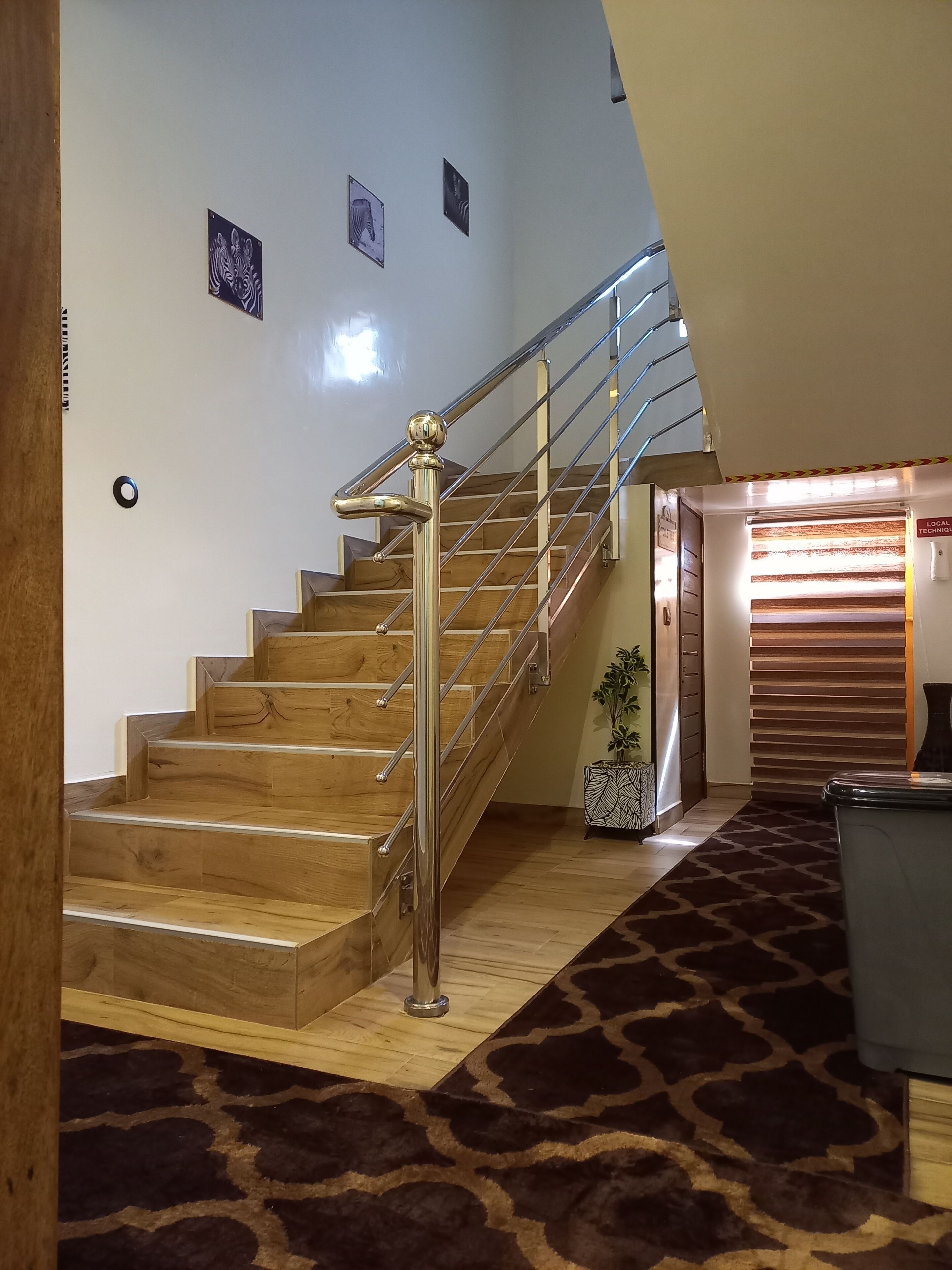 A staircase with wooden steps and a metal handrail, leading to a room with a patterned carpet and a door labeled "LOCAL TECHNIQUE."
