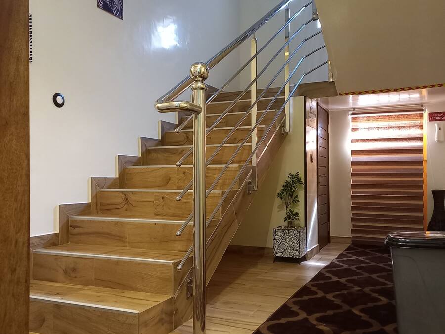 Una escalera de madera con barandilla metálica que lleva a una habitación con alfombra estampada y una puerta con la etiqueta “LOCAL TECHNIQUE”.