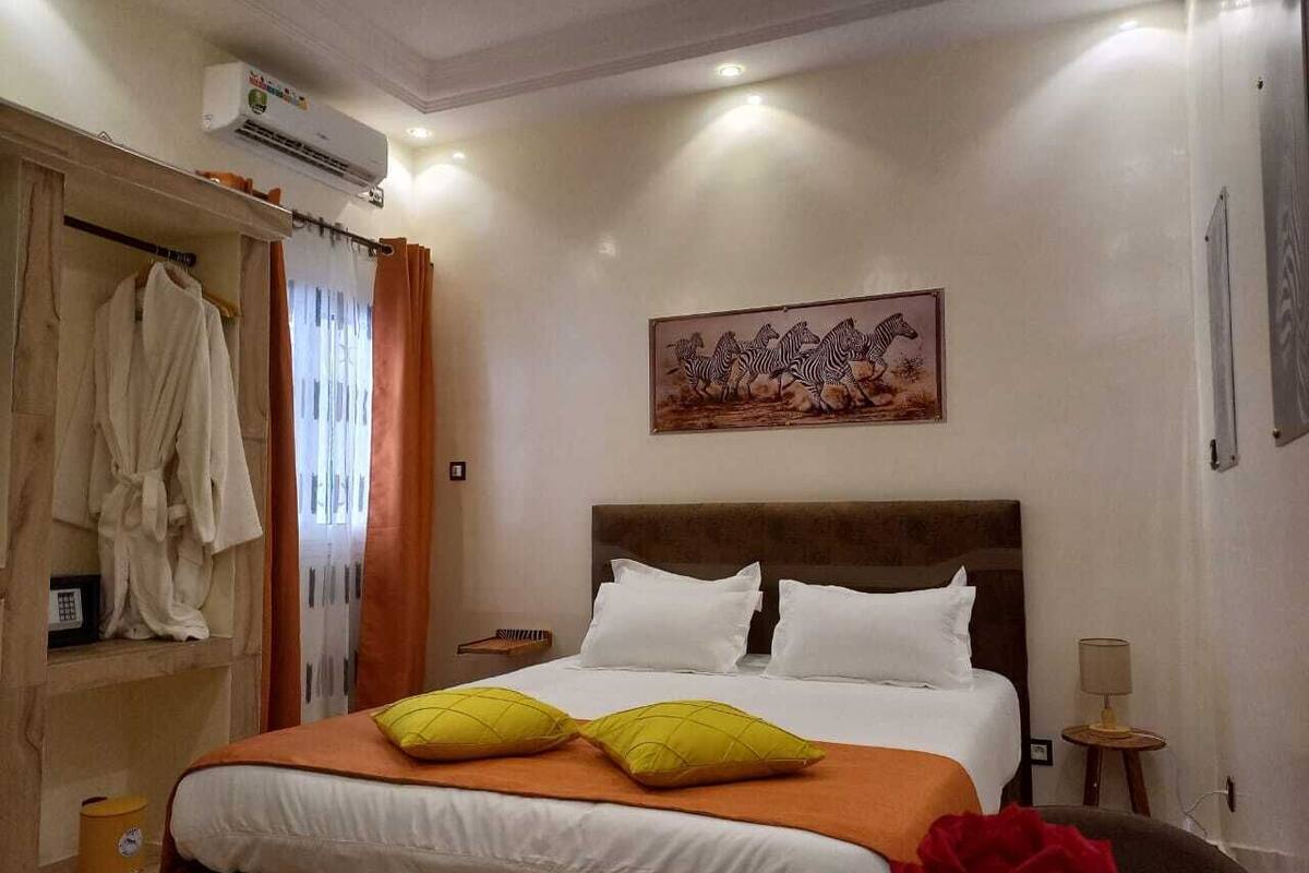 A hotel room with a bed, a wardrobe, a painting, and an air conditioning unit.