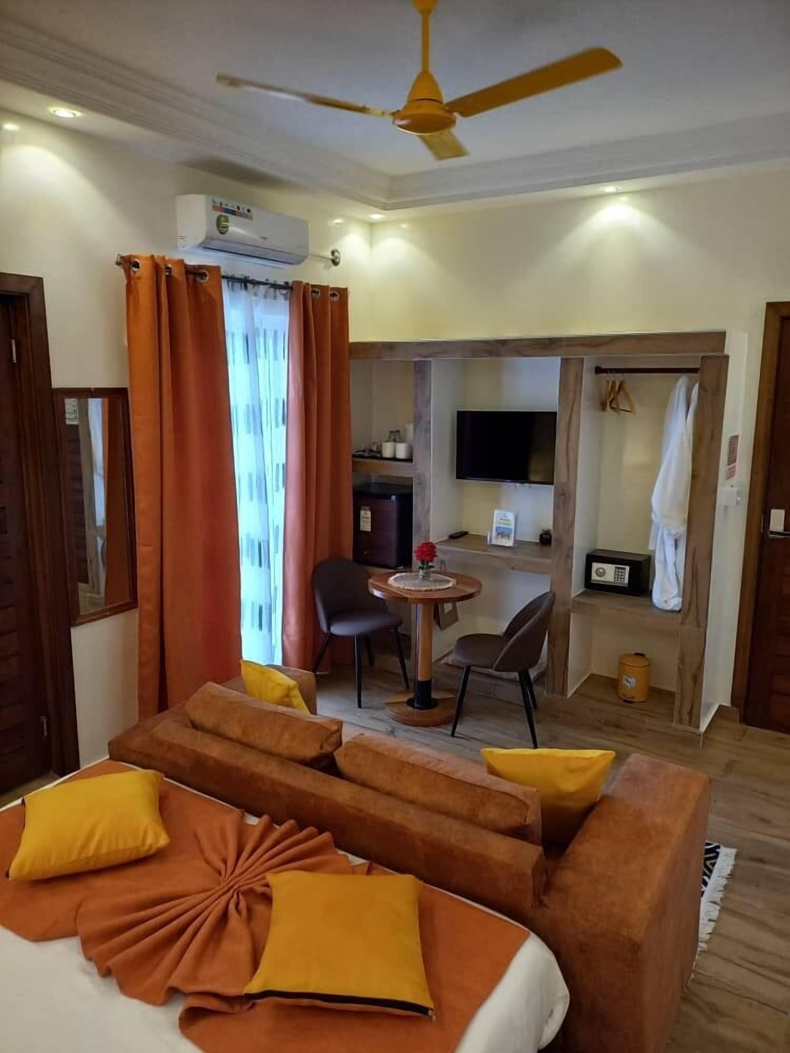 Une chambre d’hôtel comprenant un lit, un coin salon avec une table et des chaises, un téléviseur et un ventilateur de plafond.
