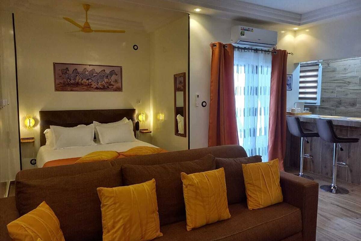 A hotel room with a bed, a sofa, a dining area, and a ceiling fan.