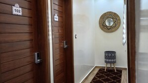 A hallway with two wooden doors labeled 101 and 102, a patterned carpet, a small table with a patterned stool, and a wall-mounted mirror. - ZEBRA RESIDENCE (Bambylor)