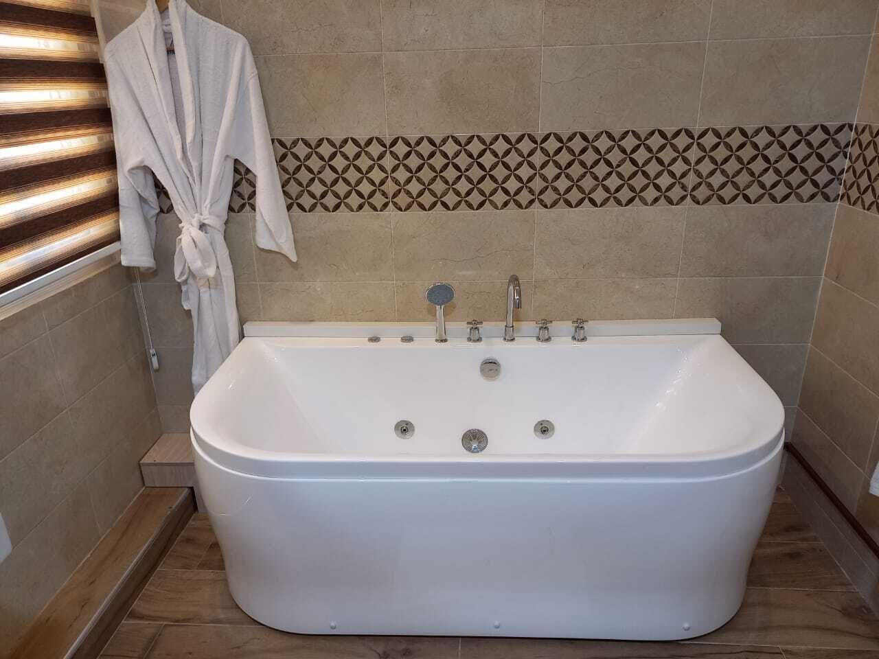 A bathroom with a freestanding bathtub, a towel rack, and patterned tiles on the wall.
