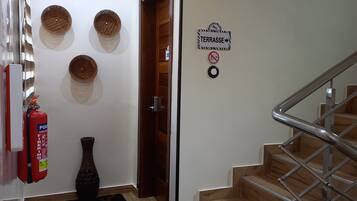 Un pasillo con escaleras de madera, un extintor, un florero y cestas fijadas a la pared.