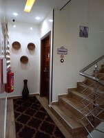 Un pasillo con escaleras de madera, un extintor, un florero y cestas fijadas a la pared.