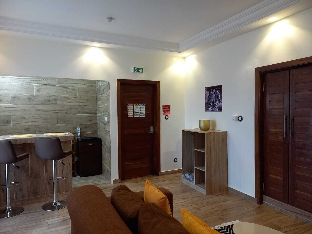 A modern hotel lobby with a bar area, a wooden reception desk, and a seating area with a brown sofa and cushions.