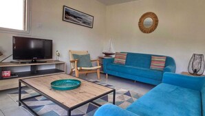 A living room with a blue sofa, a television, a wooden coffee table, and a patterned floor.
