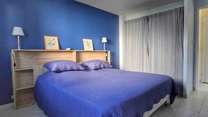 A bedroom with a bed, two bedside lamps, a headboard, and a window with curtains.
