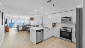 A modern kitchen with white cabinets, stainless steel appliances, and a large island with a dishwasher. - NEW 15th Floor Gulf View - Balcony - Pool - Hot Tub (Pensacola Beach)