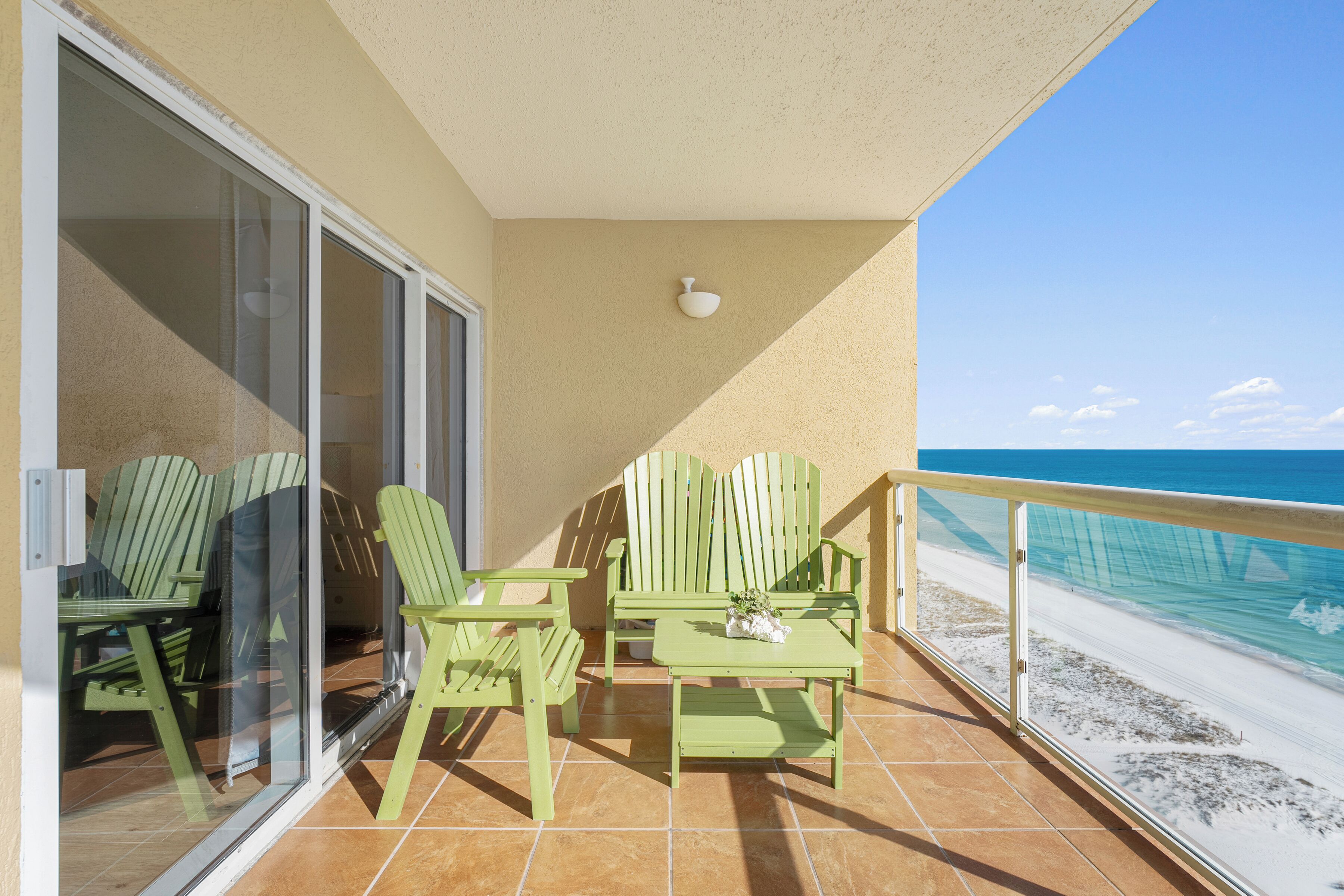 Een balkon met groene stoelen en een tafel, uitkijkend op een strand.