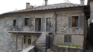A two-story stone building with a balcony, a small garden area, and a staircase leading to the upper floor.