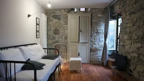 A room with a bed, a small table, a cabinet, and a stone wall.
