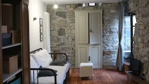 A room with a bed, a wooden cabinet, a stone wall, and a television.