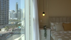 A hotel room with a large window, a bed with white bedding and polka dots, a bedside plant, and a hanging light fixture.