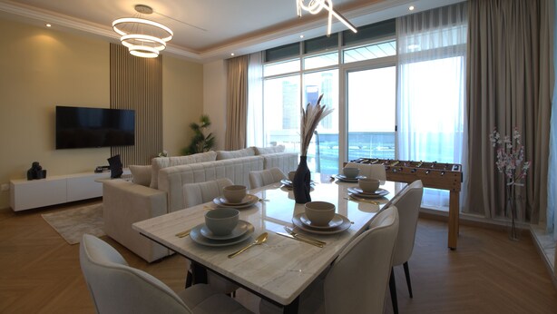 A modern living room with a sofa, dining table set for four, and a flat-screen TV mounted on the wall.