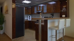 A modern kitchen with wooden cabinets, a stainless steel refrigerator, a coffee machine, and two white bar stools.