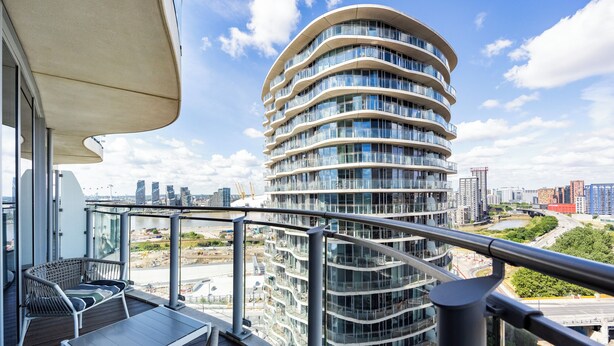 Ein modernes Gebäude mit einer gewölbten Fassade, einem Balkon mit Sitzmöbeln und Blick auf die Stadtlandschaft.