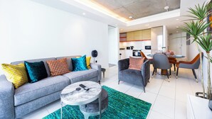 Ein modernes Wohnzimmer mit einem grauen Sofa, farbenfrohen Kissen, einem runden Couchtisch und einem Essbereich mit grauen Stühlen.