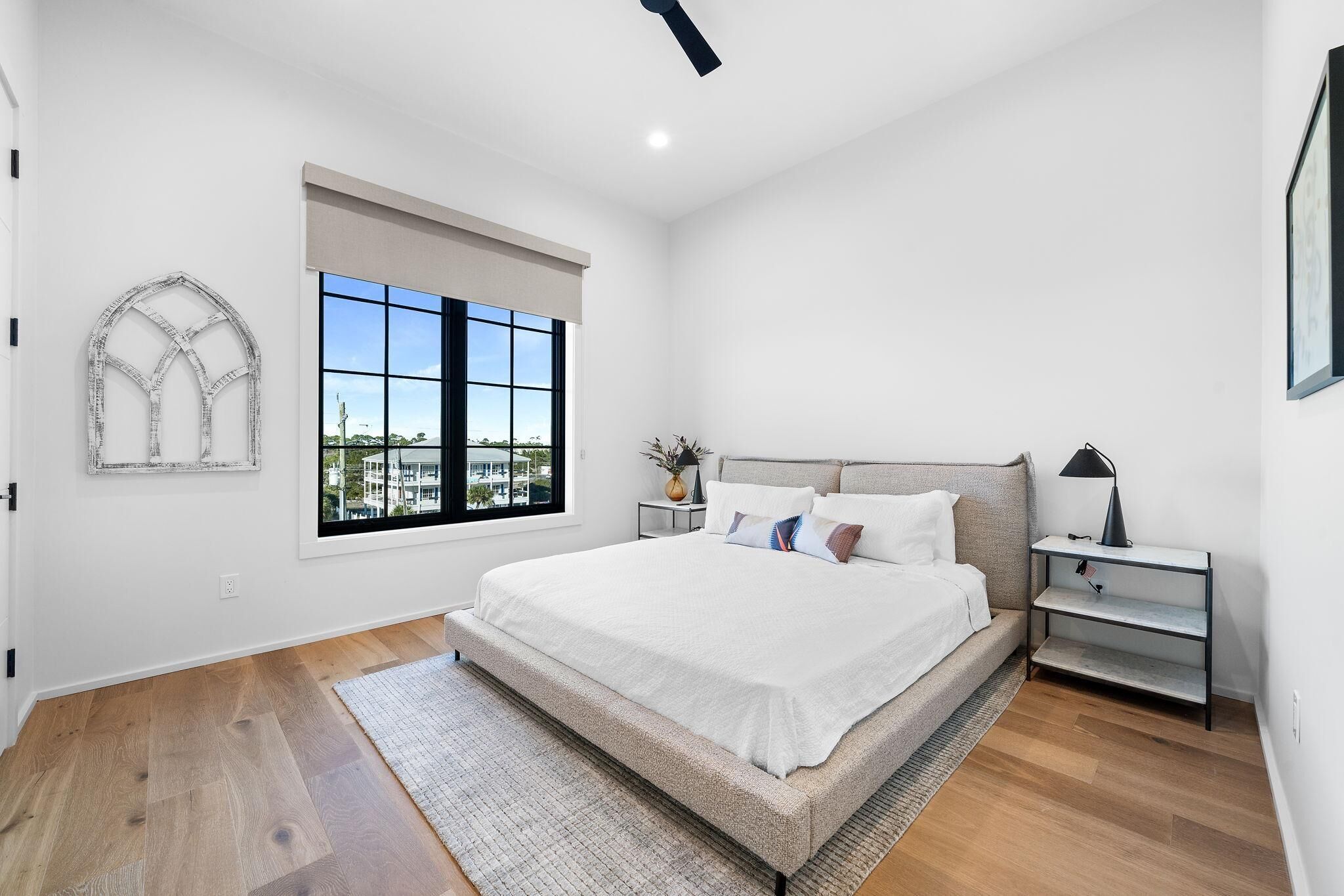 Un dormitorio moderno con una cama grande, una ventana con vistas, una mesita de noche con una lámpara y un adorno en la pared.