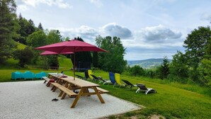 An outdoor seating area with picnic tables and chairs, a red umbrella, and a view of the countryside. - La Belle Vue, Country house Vosges ( Plainfaing) (Plainfaing)