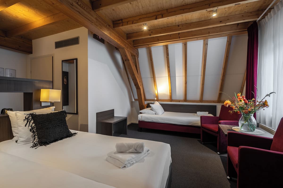 Habitación de hotel con una cama grande, una cama más pequeña, un escritorio, una silla y una ventana con cortinas.