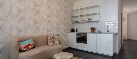 Una cocina moderna con armarios blancos, horno empotrado y cafetera.