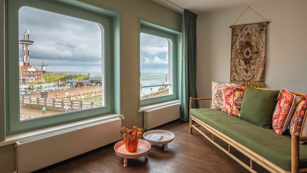Une chambre avec vue sur un phare et une plage, un canapé vert et une petite table agrémentée de fleurs.