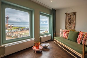 A room with a view of a lighthouse and beach, a green sofa, and a small table with flowers. - Boutique Hotel Maldegem (Vlissingen)