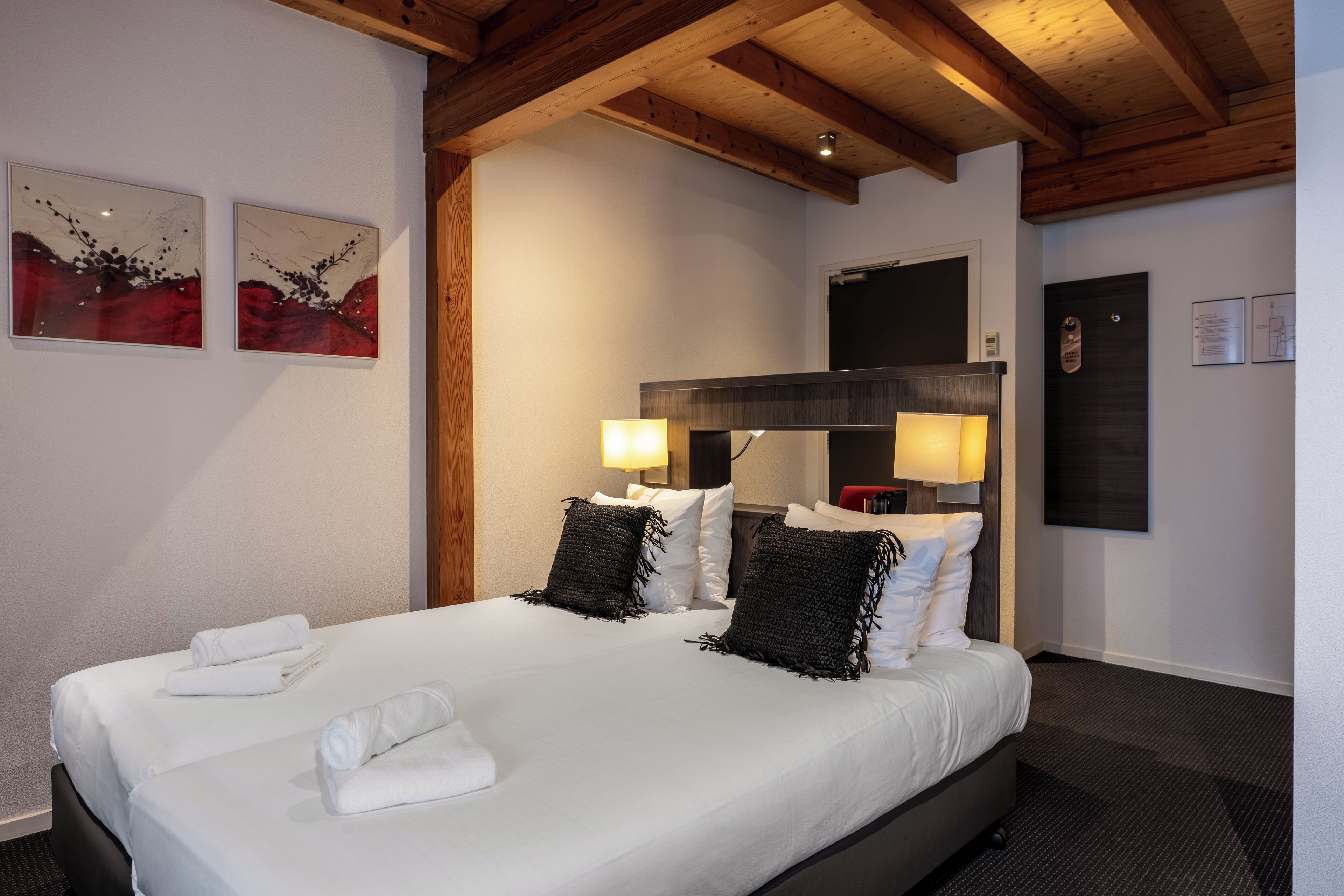 Ett hotellrum med en stor säng, två sänglampor och konstverk på väggen.