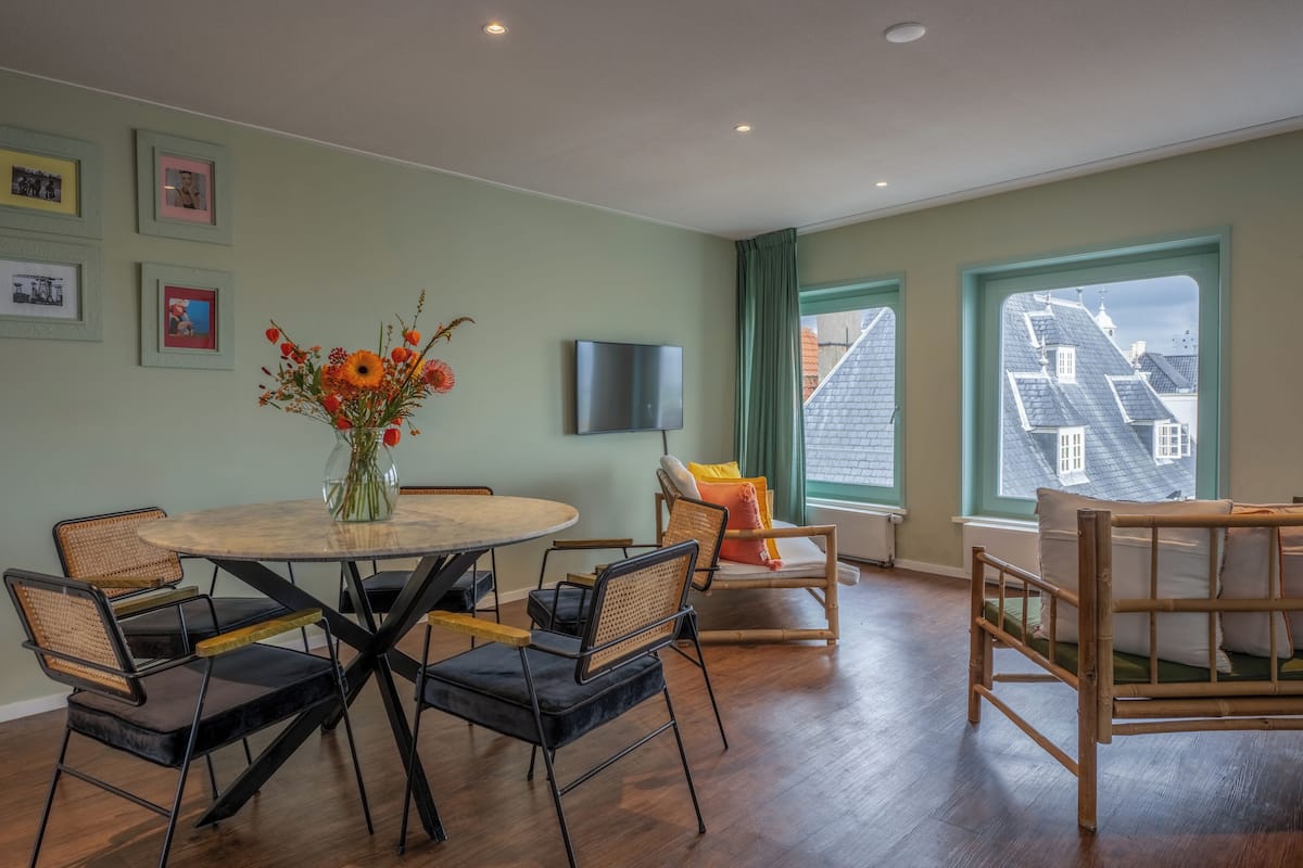 Una habitación con una mesa de comedor redonda, cuatro sillas, un televisor montado en la pared y una cama con vistas a la ciudad.