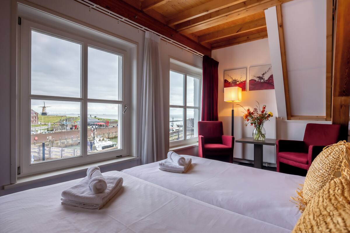 Habitación de hotel con dos camas, una mesa con lámpara y vista a un molino y un canal.