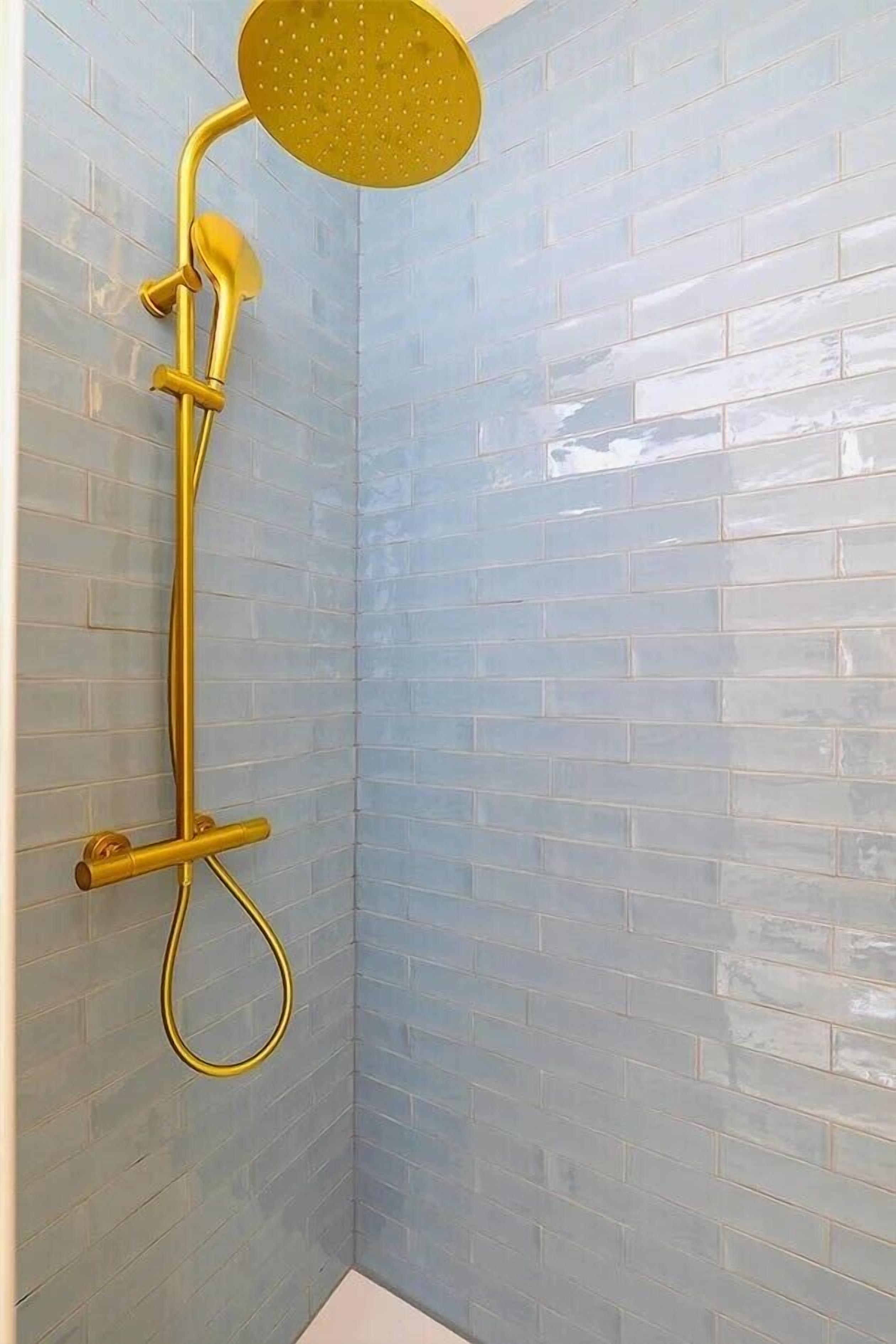 Une douche dotée d’un pommeau de douche doré et d’un flexible de douche, le tout installé sur un mur carrelé.