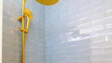 Une douche dotée d’un pommeau de douche doré et d’un flexible de douche, le tout installé sur un mur carrelé.