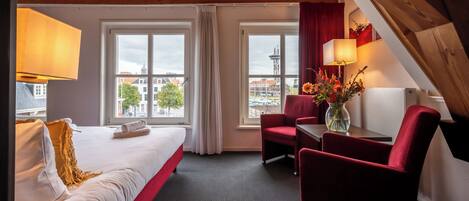 Una camera d'hotel con un letto, due finestre, una scrivania con una sedia e vista sugli edifici circostanti.