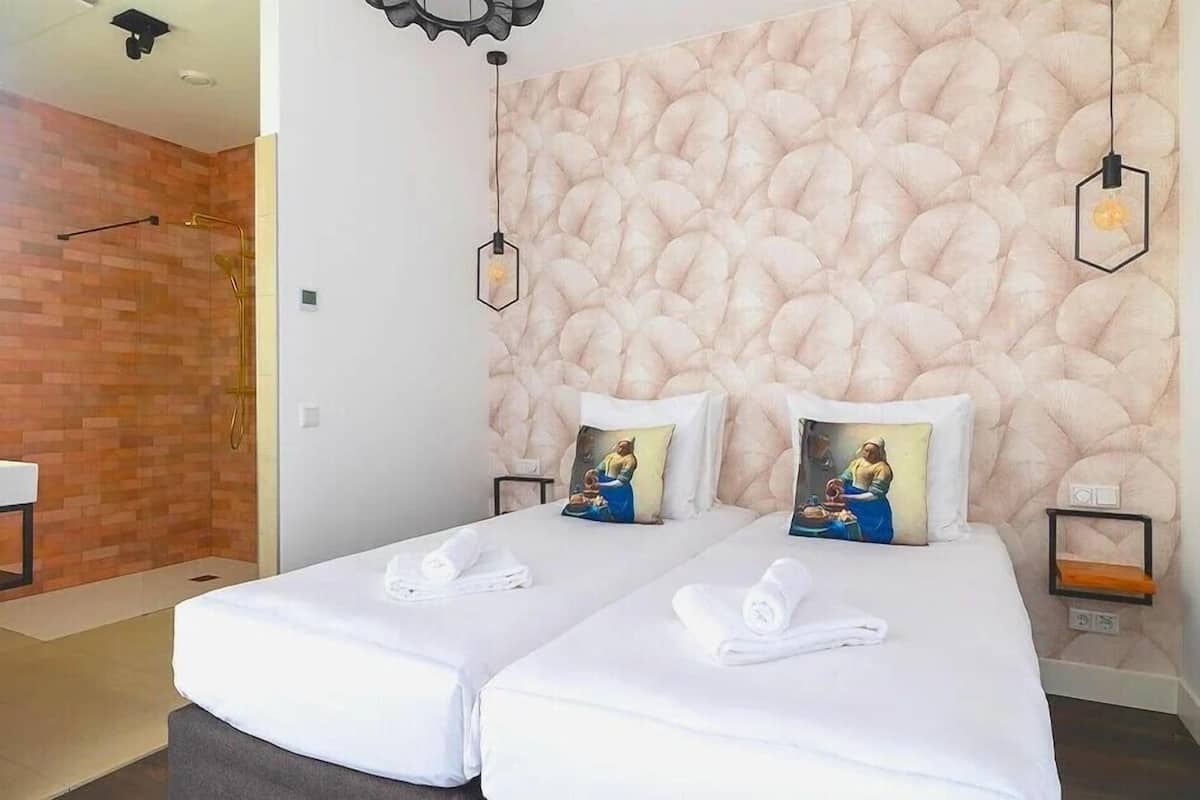Habitación de hotel con dos camas, una pared texturizada, una mesita pequeña y una lámpara colgante.