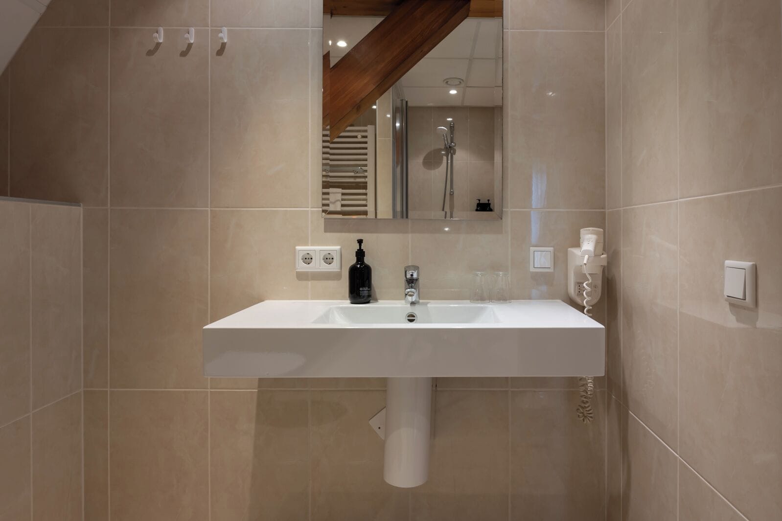 Een moderne badkamer met een wit wastafelmeubel, een spiegel erboven en een douche die op de achtergrond zichtbaar is.