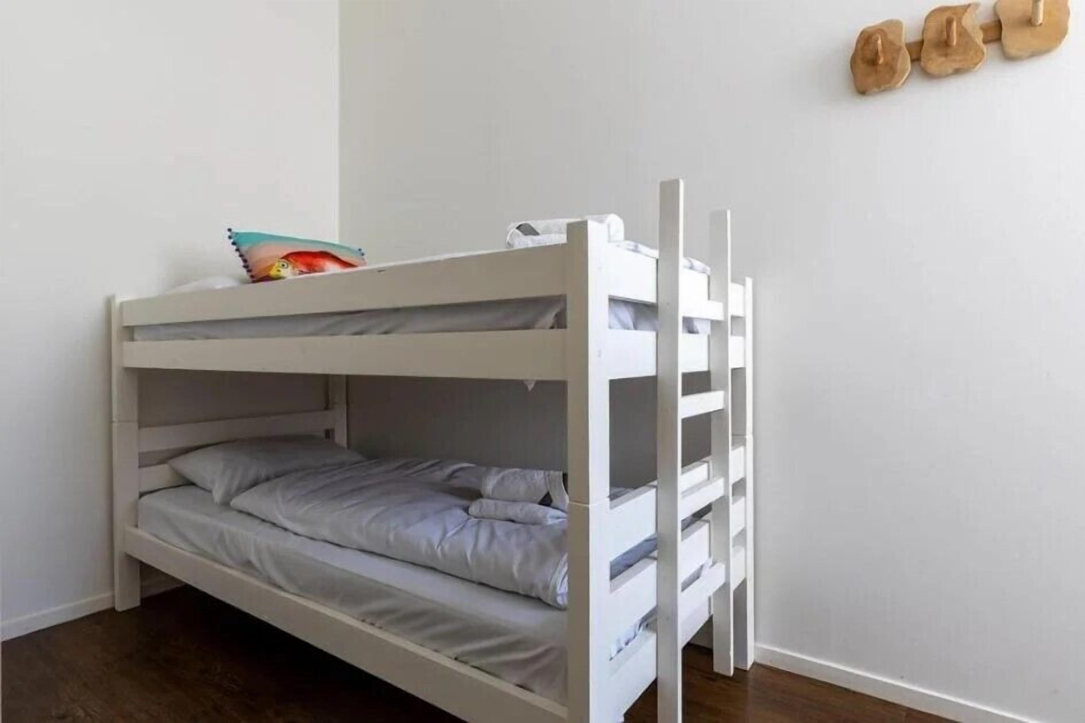 Una cama litera con una cama inferior y una superior, una almohada en la cama inferior, y un estante en la pared con una bolsa.