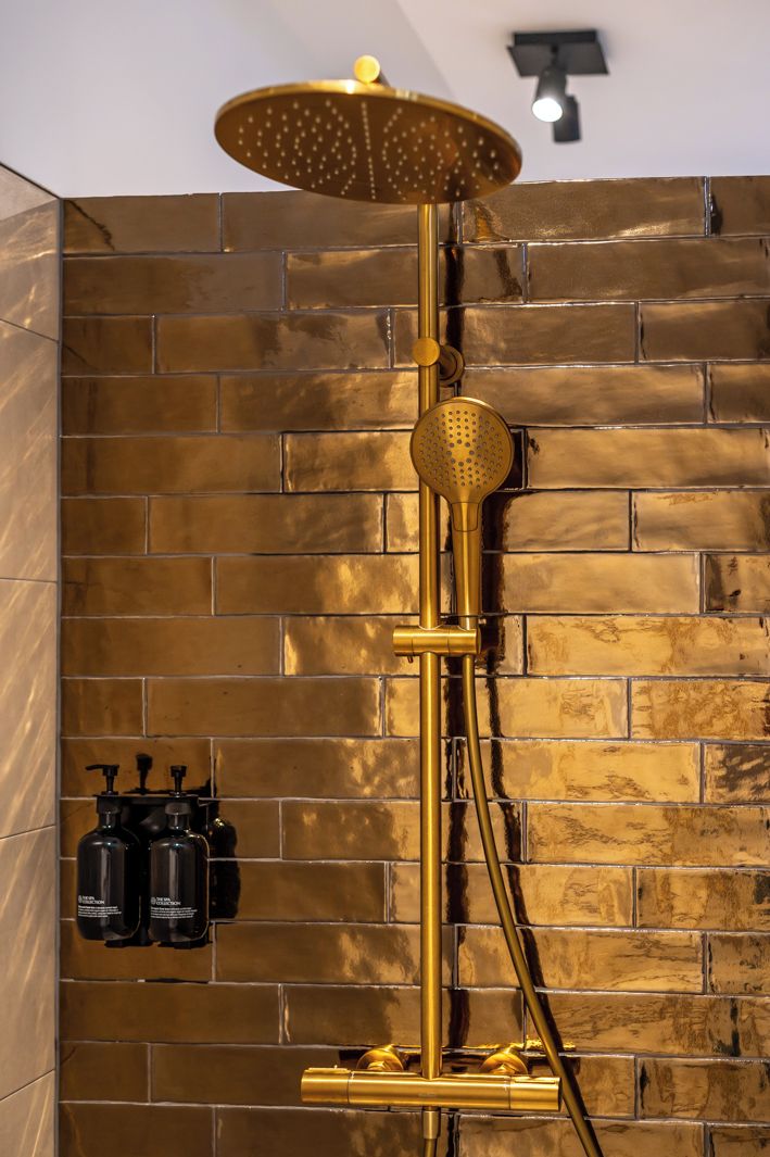A shower with a golden finish and a modern design, set against a brick wall.