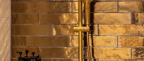 A shower with a golden finish and a modern design, set against a brick wall.