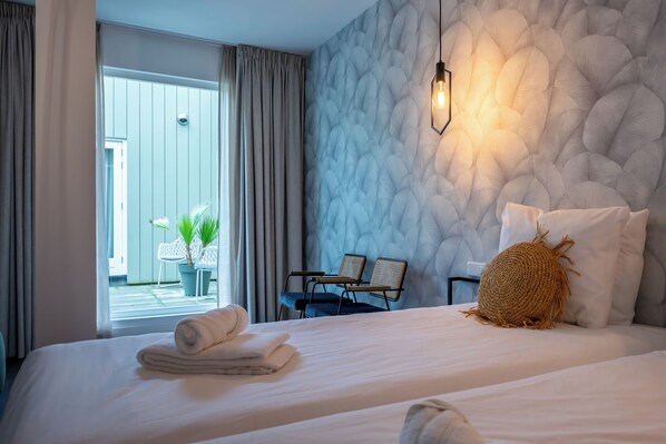 Une chambre d’hôtel avec un lit, deux chaises, une petite table, une plante en pot et une vue sur l’extérieur.