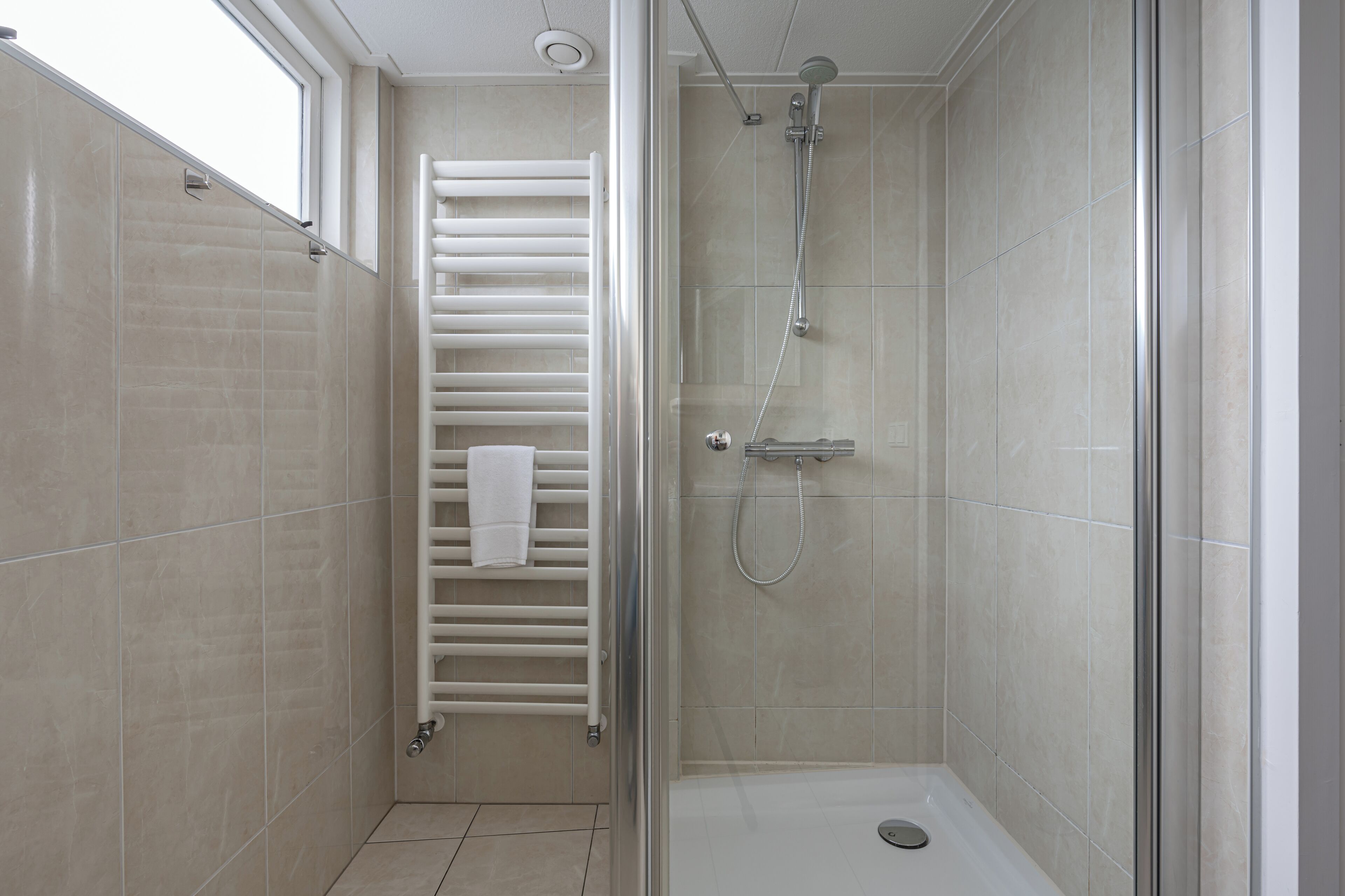Una doccia moderna con porta in vetro, un asciugamano bianco appeso al muro e soffione visibile.