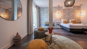 Une chambre d’hôtel moderne avec un grand lit, un canapé, une table basse ronde et un vase décoratif.