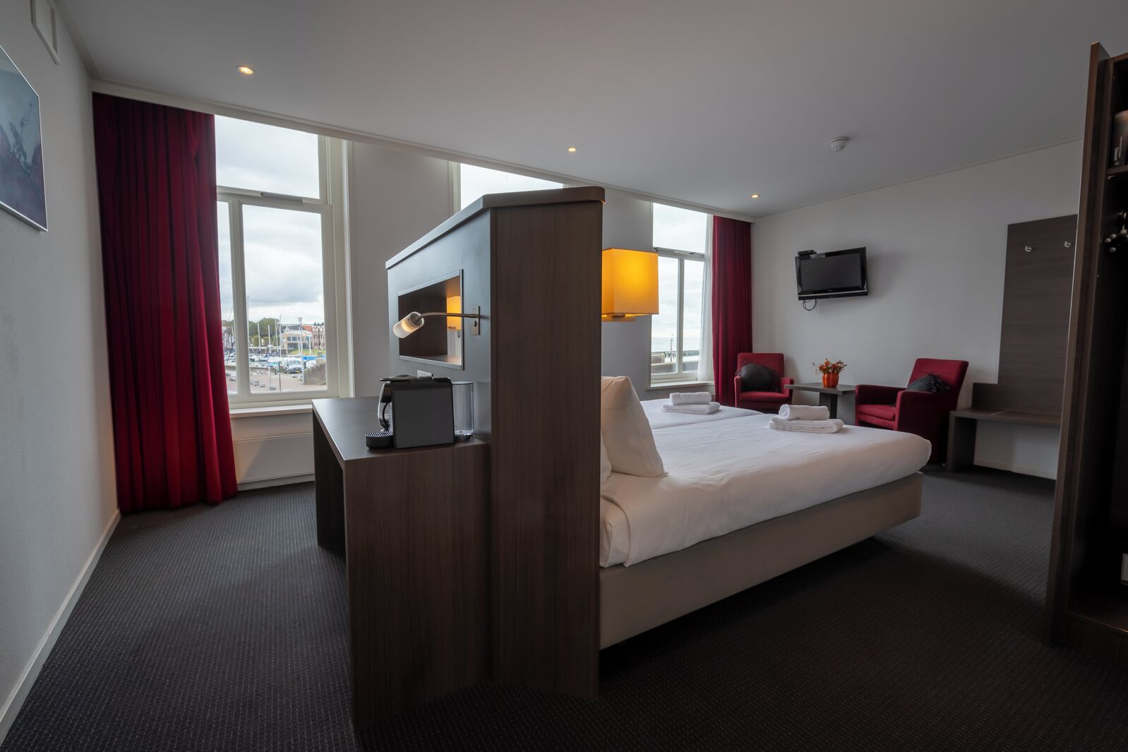 Une chambre d’hôtel équipée d’un lit, d’un bureau avec une machine à café, d’une télévision et d’une fenêtre donnant sur l’extérieur.