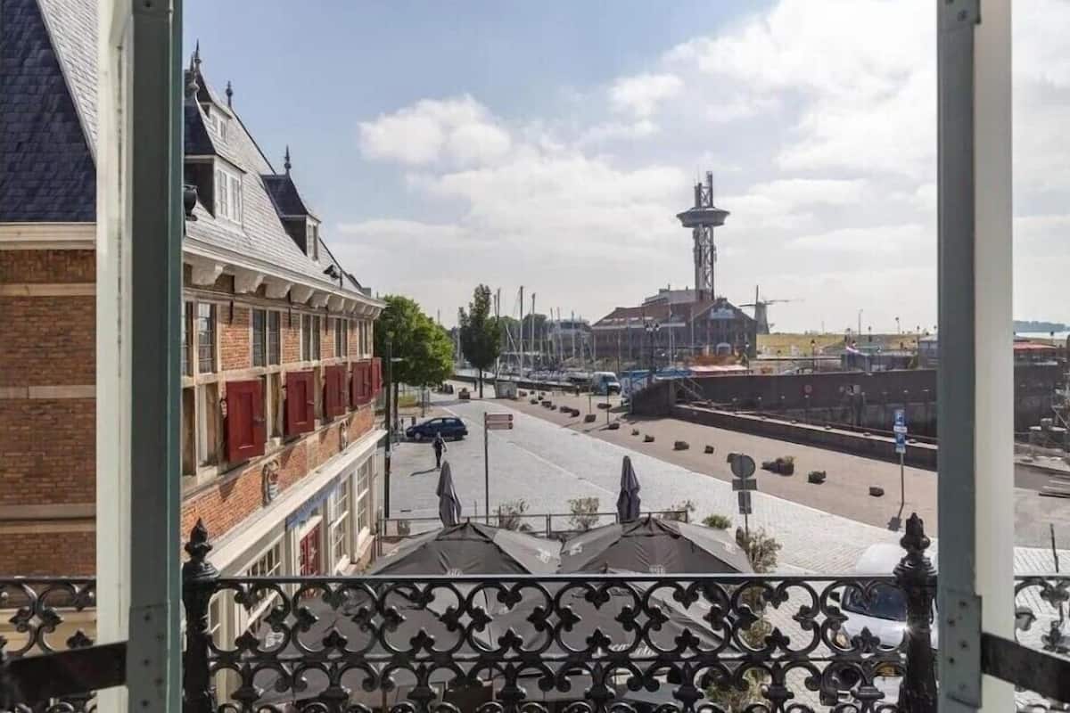 Vista desde un balcón con vista a una calle que muestra un edificio histórico, una torre y un cielo despejado.