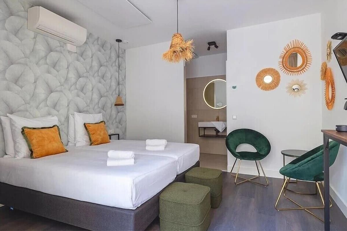 Un dormitorio moderno con una cama grande, otomanas verdes, un espejo redondo y un aire acondicionado de pared.