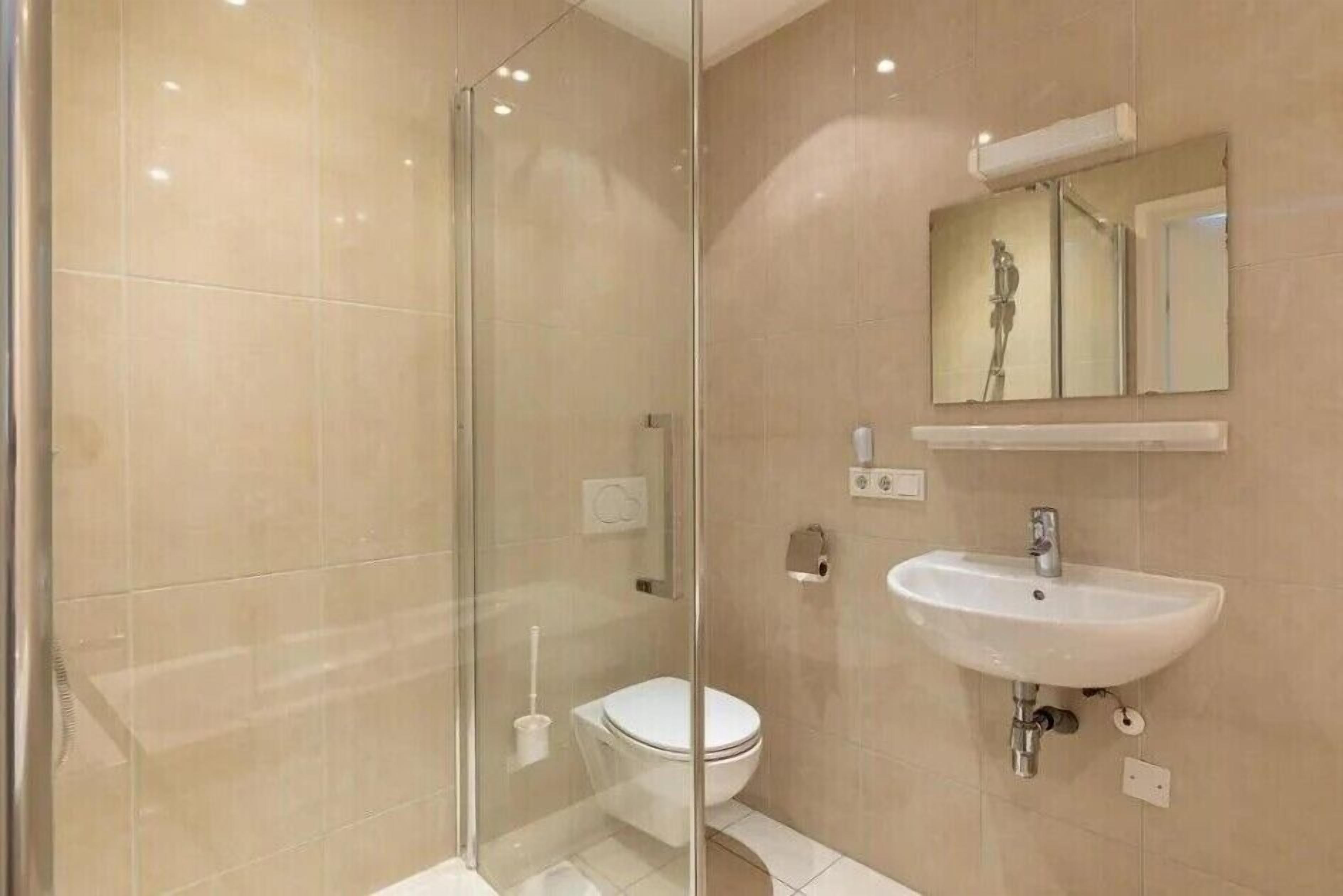 A modern bathroom with a glass shower enclosure, a white sink, and a toilet.