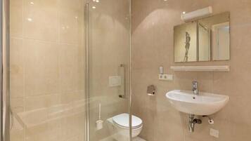 Een moderne badkamer met een douchecabine van glas, een wit wastafelmeubel en een toilet.